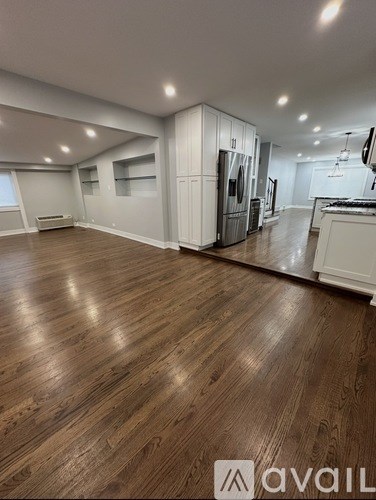A spacious room with wooden flooring and a kitchen area in the background.