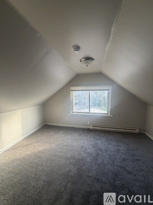 A carpeted attic room with a window and a light on the ceiling.