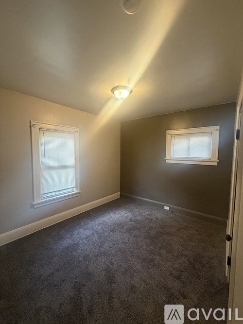 A room with a carpeted floor and two windows.