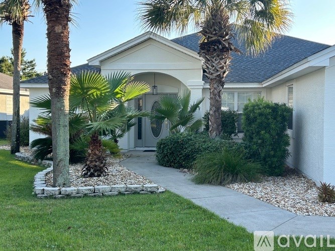 A house with a front yard featuring a palm tree and a small garden.