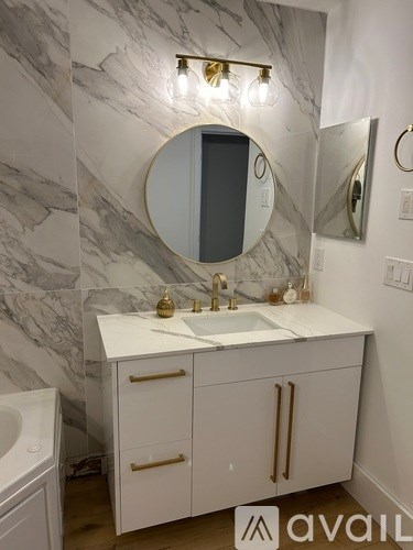 A bathroom with a marble wall and a round mirror above a sink.