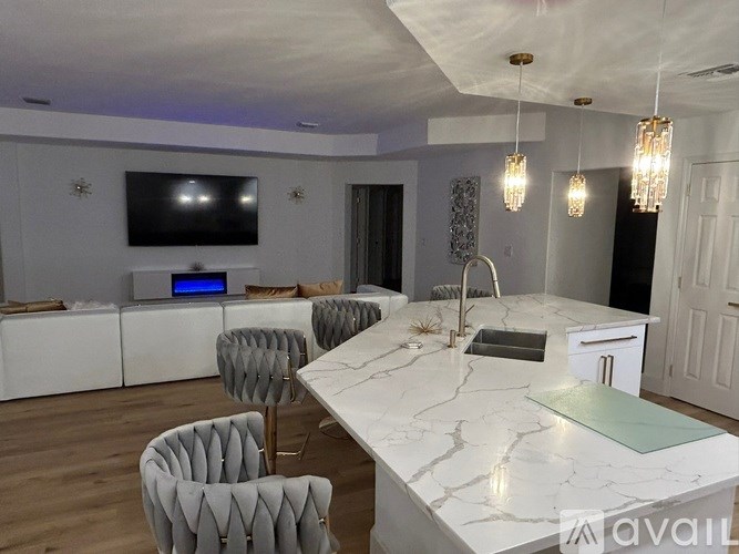 A modern kitchen with a white marble countertop and grey chairs.