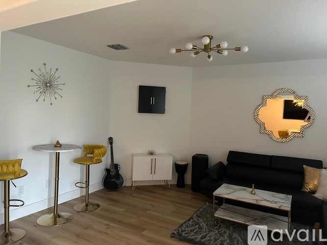 A living room with a black couch, a guitar, and a mirror on the wall.