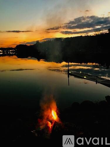A campfire burns in the foreground of a serene lake at sunset.