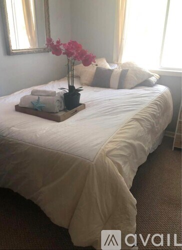 A bed with white sheets and a tray with a plant and towels on it.