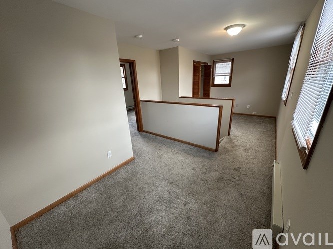 A spacious room with a carpeted floor and a window with blinds on the right side.