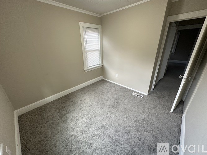 A carpeted room with a window and a door leading to another room.