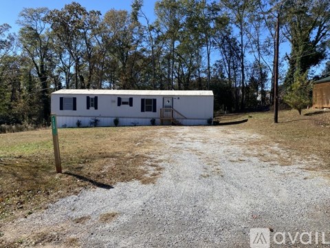 A white trailer is parked in a gravel lot with trees in the background.