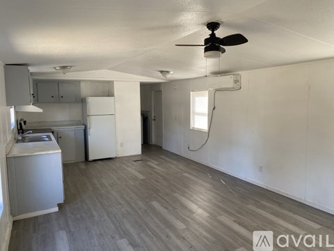 A room with a fan and a kitchen area with cabinets and a sink.