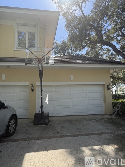A basketball hoop stands in front of a yellow house with a car parked in the driveway.