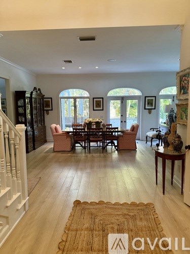 A living room with a brown rug and a dining table with chairs.