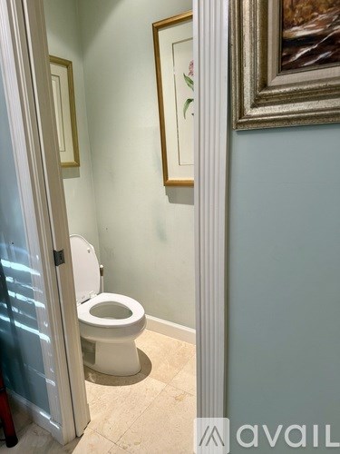 A white toilet is in a bathroom with a painting on the wall.