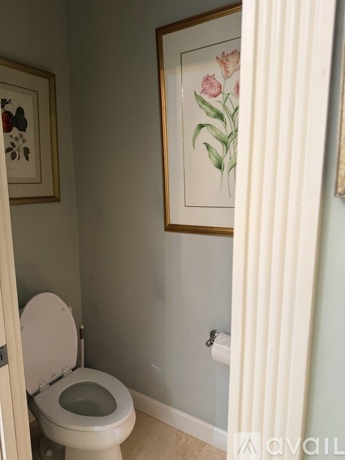 A toilet with a white seat and lid is in a bathroom with a painting of flowers on the wall.