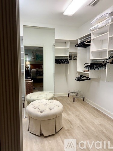 A walk in closet with clothes hanging and a bench.
