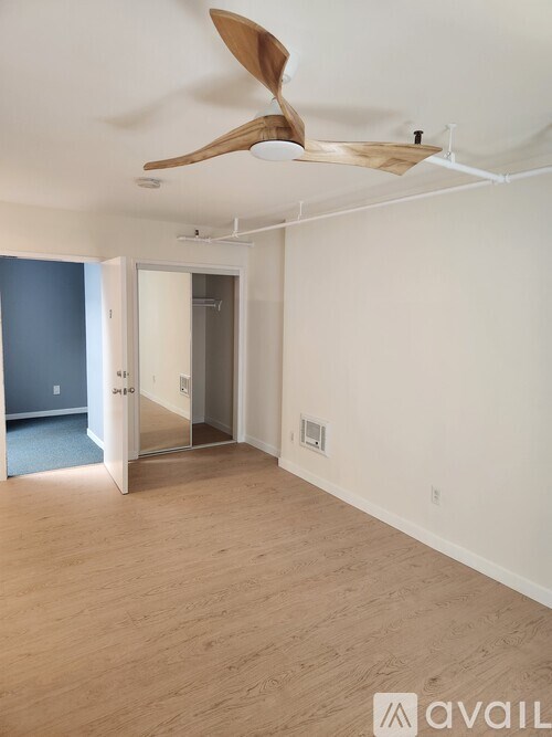 A room with a fan and wooden floors.