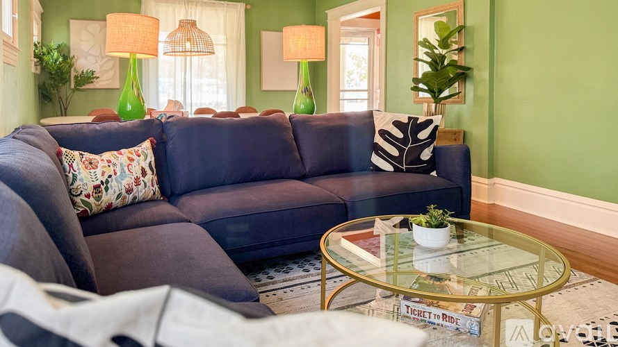 A living room with a blue couch, a glass coffee table, and a plant.
