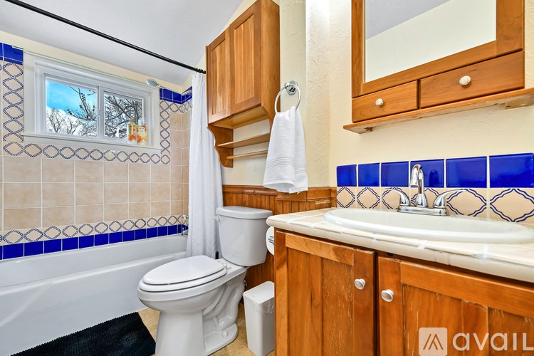 A bathroom with a white toilet, a bathtub with blue tiles, and wooden cabinets.