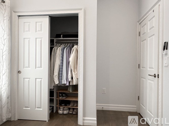 A white door is open to a closet with clothes hanging.