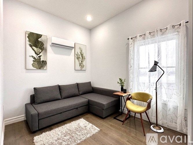 A grey couch with a yellow chair and a white rug in a room.