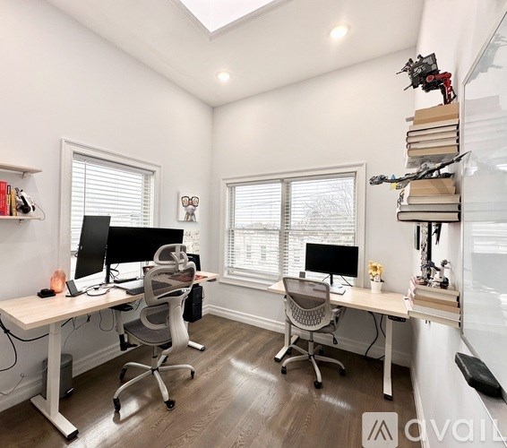 A well-lit home office with two desks and chairs, one of which has a computer on it.