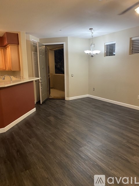 A room with wooden flooring and a kitchen area to the left.