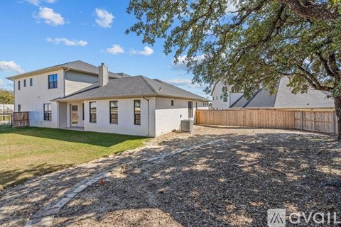 A house with a white exterior and a grey roof is surrounded by a gravel driveway and a wooden fence.