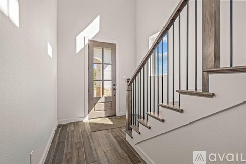 A hallway with a wooden floor and a staircase with a metal railing.