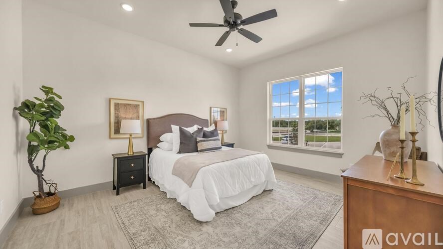 A bedroom with a large bed, a ceiling fan, and a view of the outdoors through the window.
