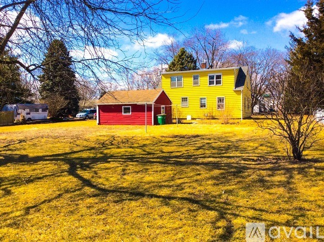 A yellow house with a red roof is surrounded by trees.