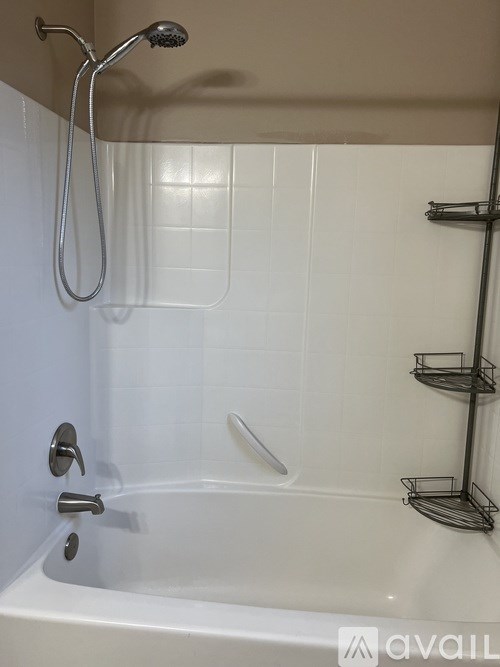A white bathtub with a shower head and a metal rack on the wall.