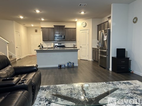 A living room with a black leather couch and a kitchen area in the background.
