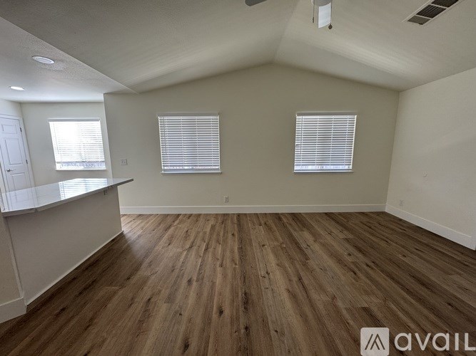 A room with wooden flooring and two windows with blinds.