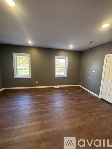 A room with wooden flooring and two windows.