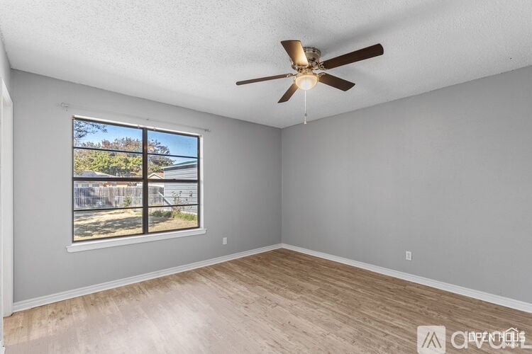A room with a ceiling fan and a window overlooking a street.