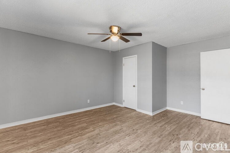 A room with a ceiling fan and light fixture, two doors, and a wooden floor.