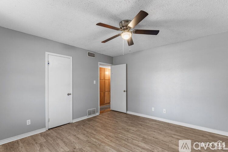 A room with a ceiling fan and light, two doors, and a wooden floor.