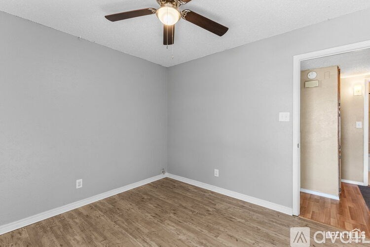A room with a ceiling fan and light fixture, and a doorway leading to another room.