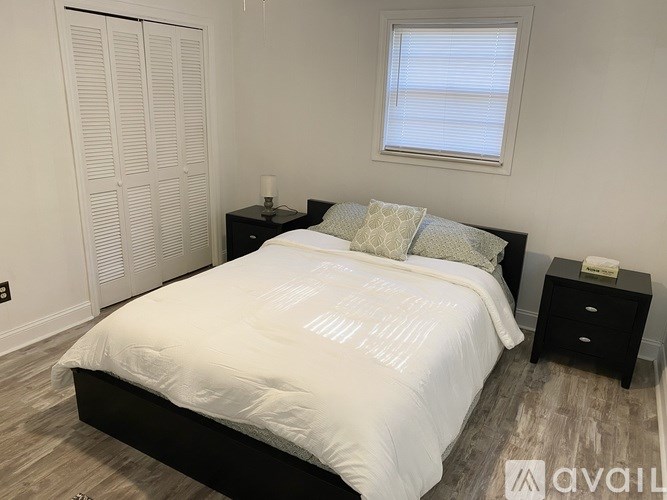 A bedroom with a bed, nightstand, and a window with blinds.