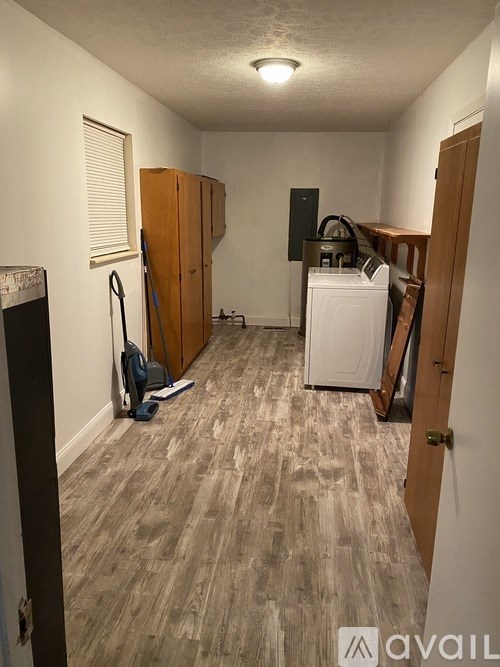 A room with a white washer and dryer, a vacuum cleaner, and a broom.