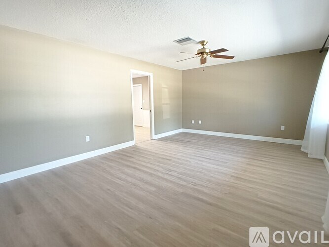 A room with a ceiling fan and light fixture, a door, and a wall with a window.