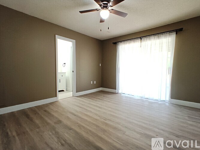A room with a ceiling fan and light, wooden floors, and a window with curtains.