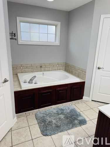 A bathroom with a white door, a window, a sink, and a blue rug.