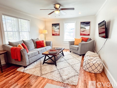 A living room with a grey couch, a white rug, and a ceiling fan.