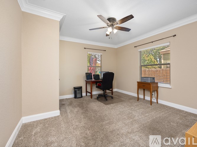 A room with a ceiling fan, a chair, a small table, and a window with blinds.