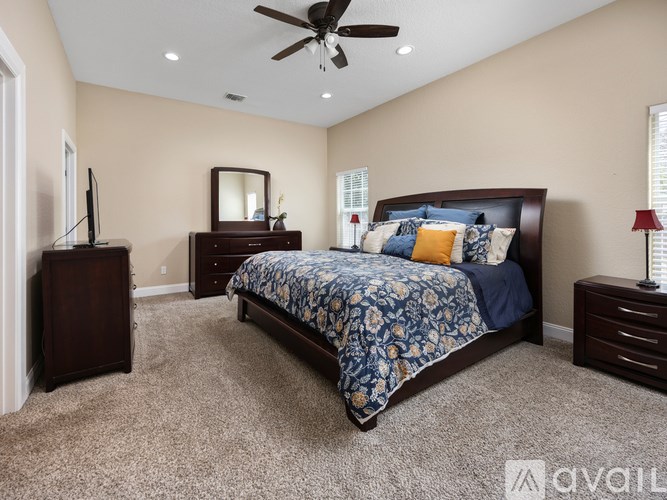 A bedroom with a large bed, a dresser, a mirror, and a ceiling fan.