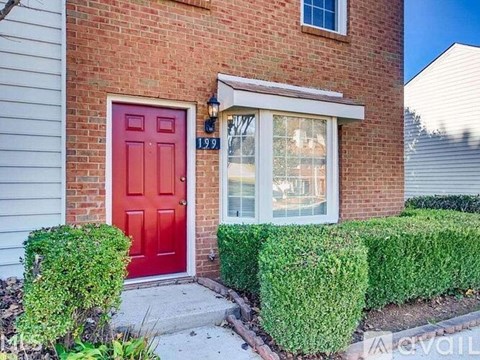 A red door is on the left side of a brick house.