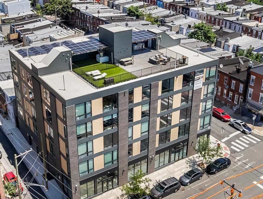 A modern building with a green roof is surrounded by other buildings and cars on the street.