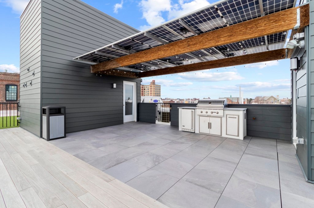 A rooftop patio with a grey wall, a wooden pergola, and a small kitchenette.