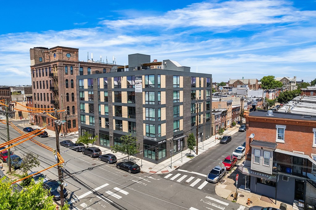 A modern glass building is situated on a street corner with cars parked along the curb.