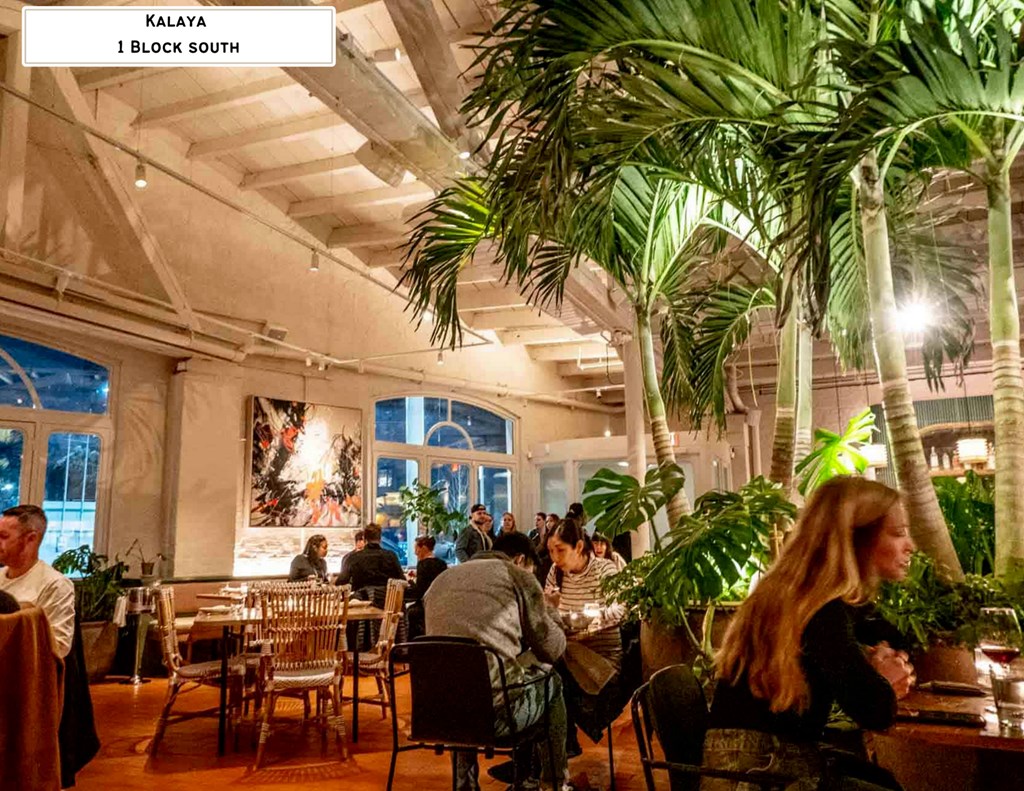A group of people are sitting at tables in a restaurant with palm trees.